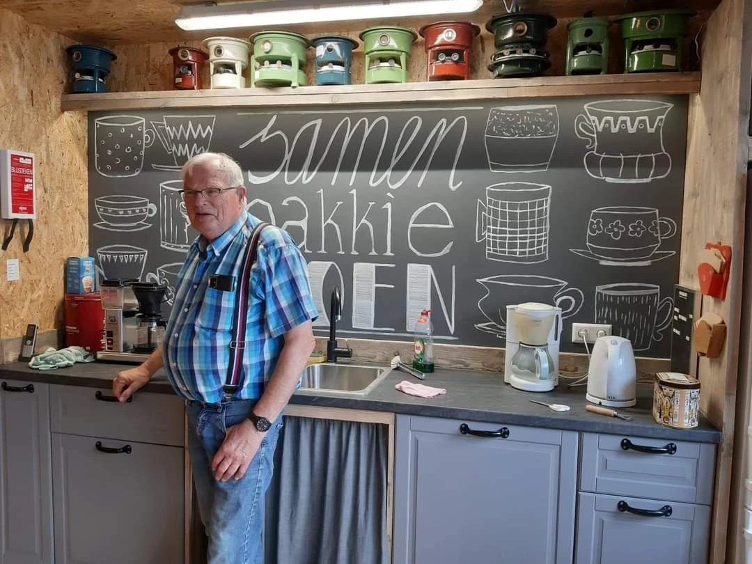 Man in blauwe geruite overhemd in een kleine keuken met krijtbord met teksten erop en huishoudelijke apparaten