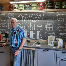 Man in blauwe geruite overhemd in een kleine keuken met krijtbord met teksten erop en huishoudelijke apparaten