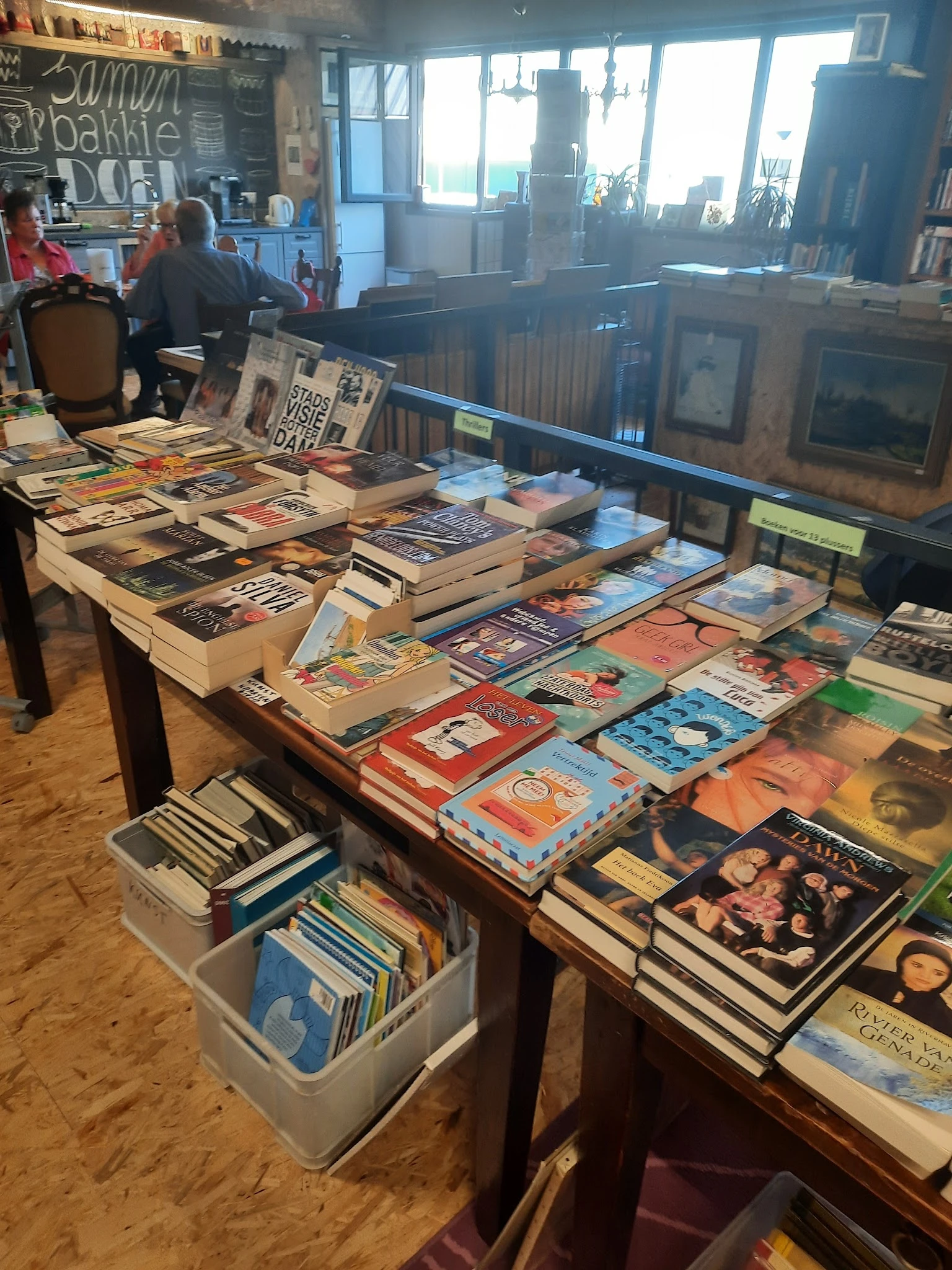 Tafels volgestapeld met tweedehands boeken, dvd's en cd's in verschillende genres en kleuren