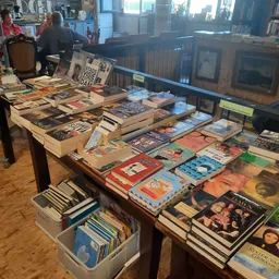 Tafels volgestapeld met tweedehands boeken, dvd's en cd's in verschillende genres en kleuren
