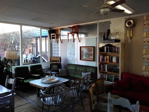 Woonkamer-achtige winkelruimte met zwarte zitmeubels, boekenrek, salontafel en grote ramen met daglicht