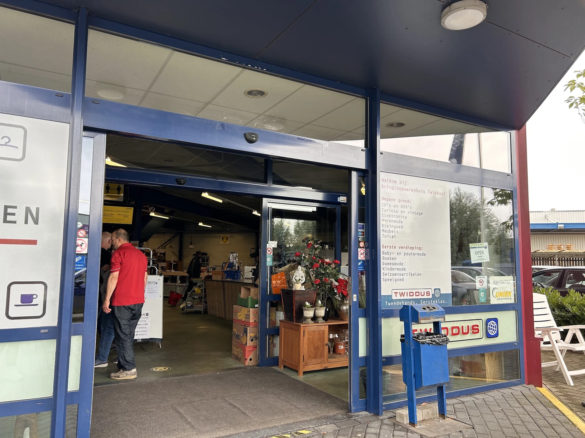 Ingang van kringloopwinkel met blauwe kozijnen, open deur en zicht op winkelinterieur met spullen
