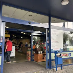 Ingang van kringloopwinkel met blauwe kozijnen, open deur en zicht op winkelinterieur met spullen