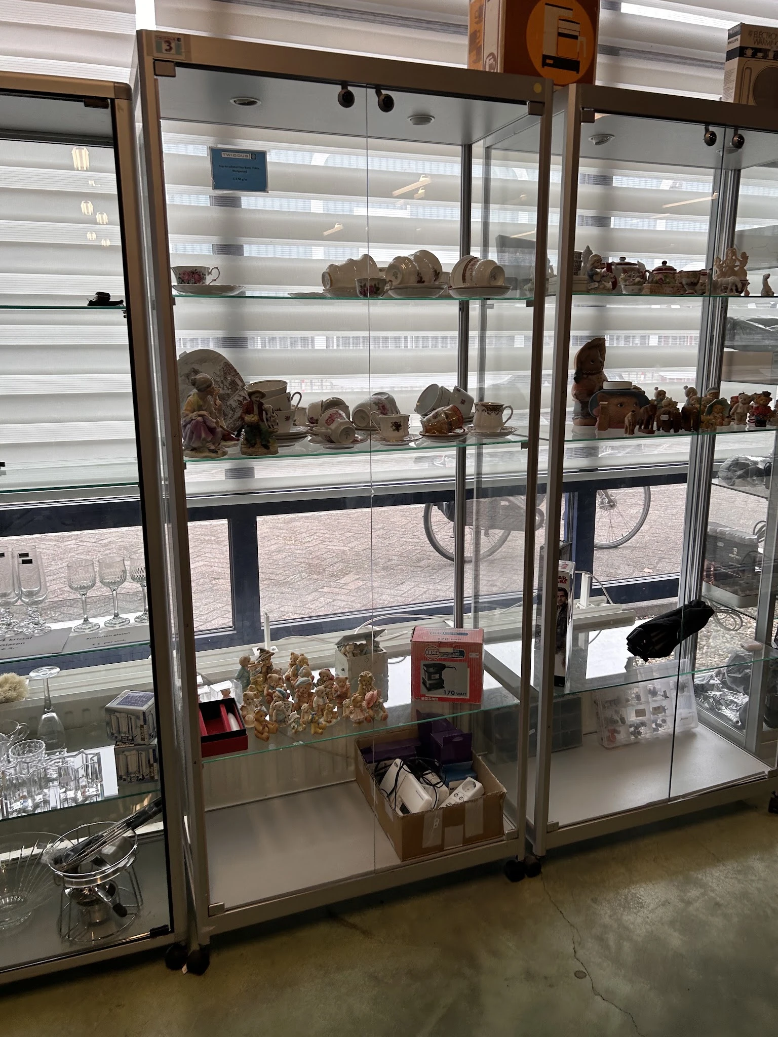 Glazen vitrinekast met aardewerk, beeldjes en decoratieve objecten uit de tweedehandswinkel