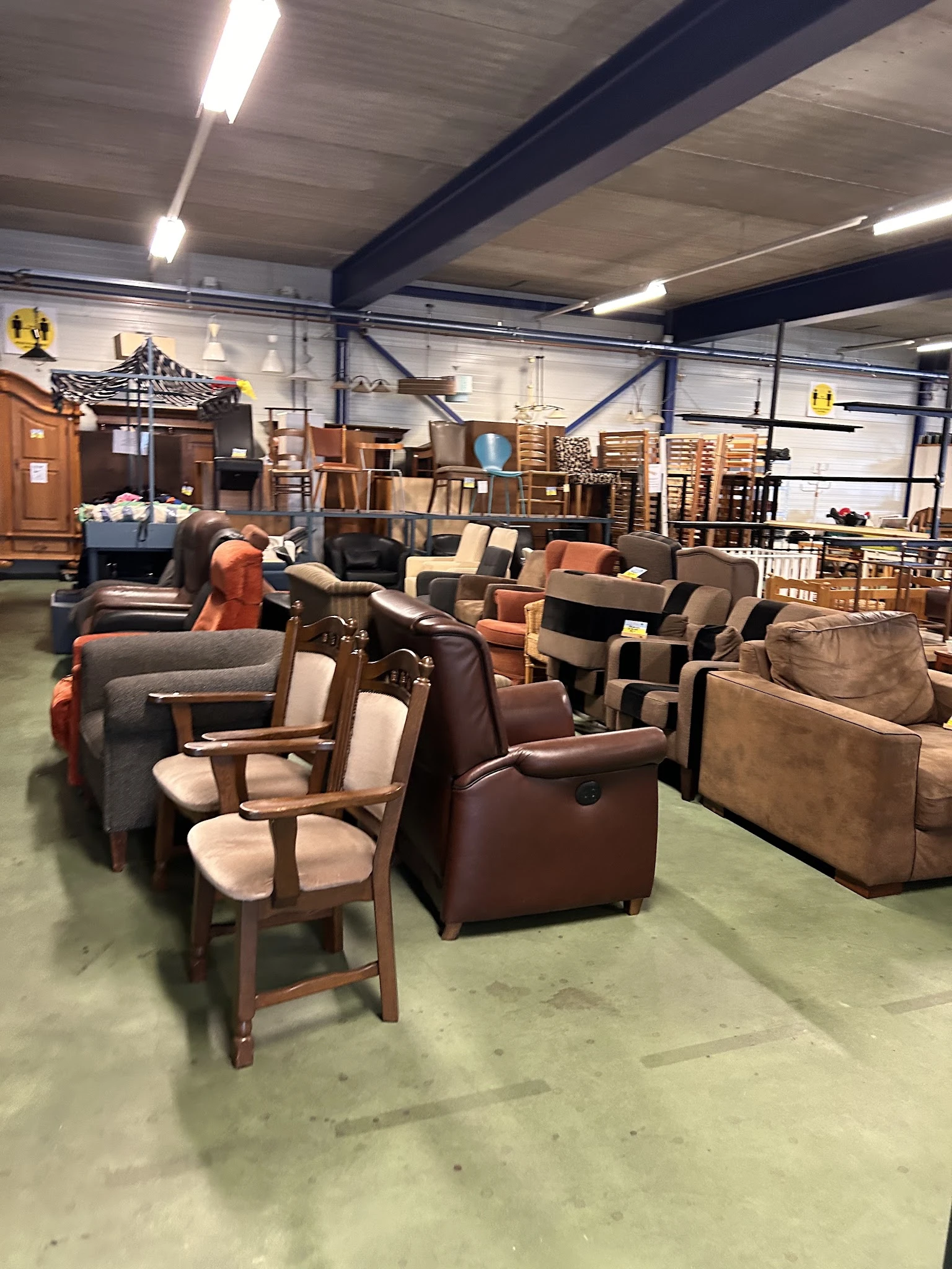 Uitgestalde meubels in een kringloopwinkel, waaronder fauteuils, stoelen en banken in verschillende kleuren en stijlen
