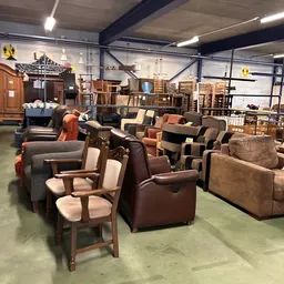 Uitgestalde meubels in een kringloopwinkel, waaronder fauteuils, stoelen en banken in verschillende kleuren en stijlen