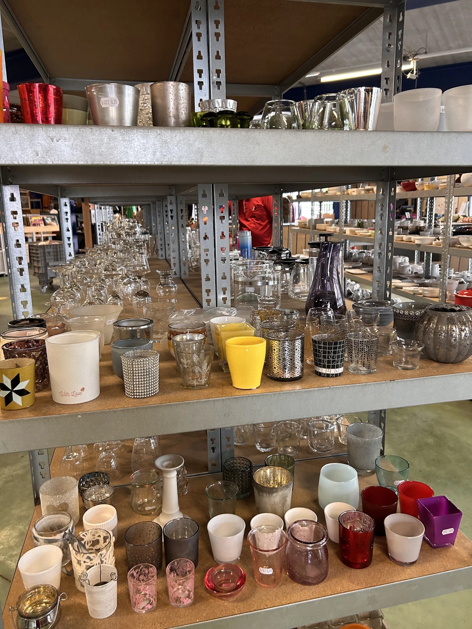 Uitgestalde glazen, kopjes en keukenartikelen op een houten balie in de kringloopwinkel
