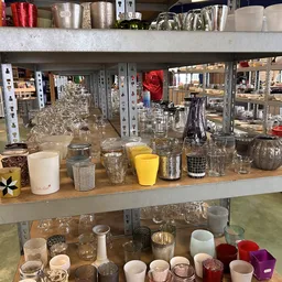 Uitgestalde glazen, kopjes en keukenartikelen op een houten balie in de kringloopwinkel