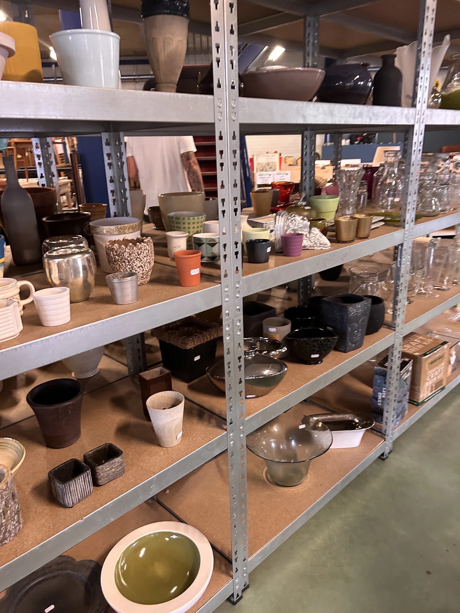 Stellingen met huishoudartikelen zoals servies, bekers, potten en keukenspullen in verschillende kleuren en materialen