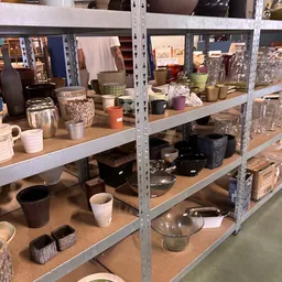 Stellingen met huishoudartikelen zoals servies, bekers, potten en keukenspullen in verschillende kleuren en materialen