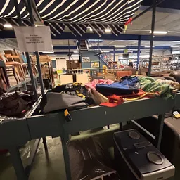 Tafel vol met kleding in verschillende kleuren in een kringloopwinkel