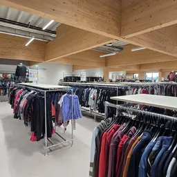 Ruime winkelhal met houten spantconstructie, rekken met tweedehands kleding langs de wanden en in het midden
