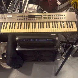 Roland synthesizer met keyboard en zwarte apparatuur eronder op grijze ondergrond
