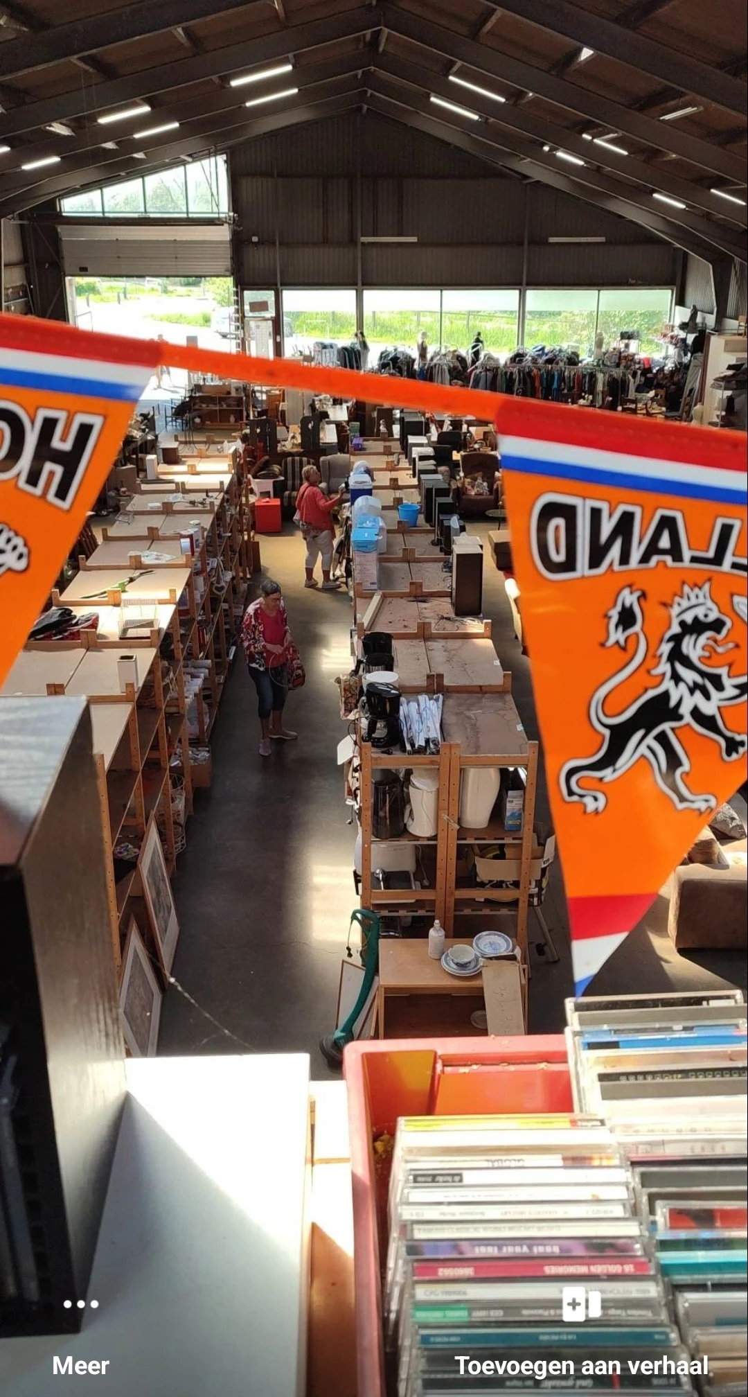 Overzicht van de winkelvloer met houten stellingen en kasten, enkele klanten lopend tussen de rekken, oranje banner met leeuw