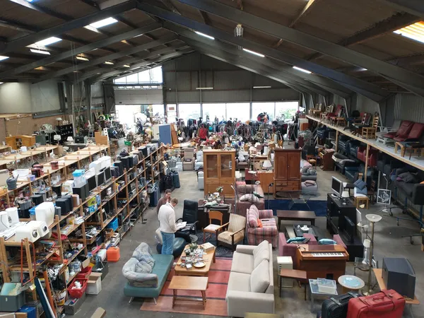 Overzicht van kringloopwinkel met meubels, huishoudelijke artikelen en spullen verspreid over de vloer en in stellingen