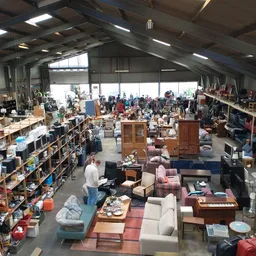 Overzicht van kringloopwinkel met meubels, huishoudelijke artikelen en spullen verspreid over de vloer en in stellingen