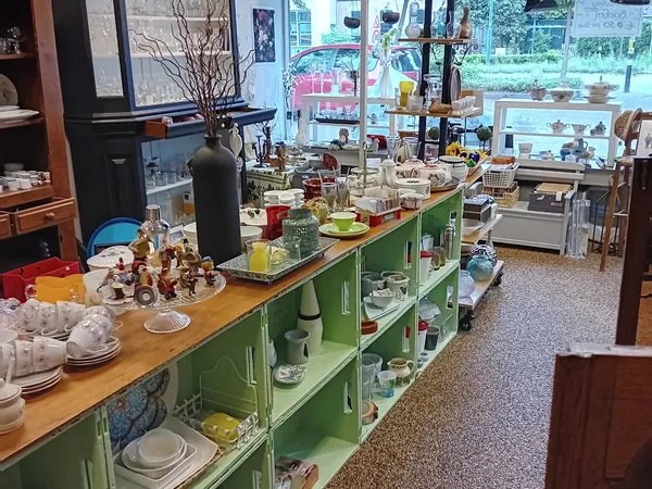 Vintage kringloopwinkel interieur met groene kasten, houten toonbank, serviesgoed en decoratieve spullen op stellingen