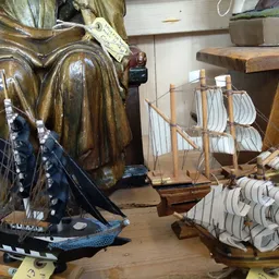 Tweedehands decoratieve items: houten scheepsmodellen en een bronzen beeld op houten voet