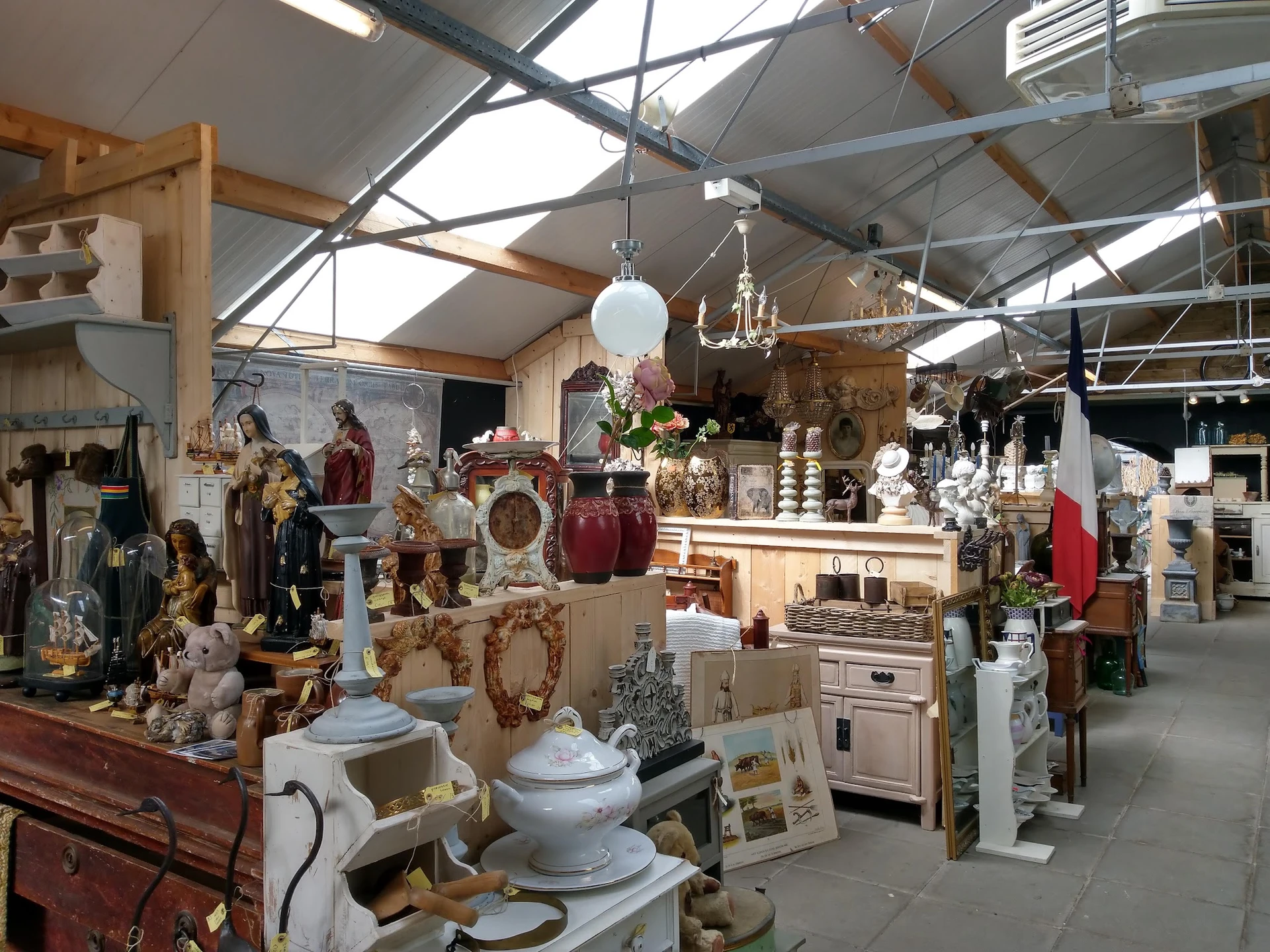 Binnenaanzicht van kringloopwinkel met stellingen vol huishoudelijke spullen, servies, beelden en decoratiestukken onder een 