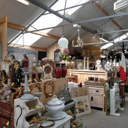 Binnenaanzicht van kringloopwinkel met stellingen vol huishoudelijke spullen, servies, beelden en decoratiestukken onder een 