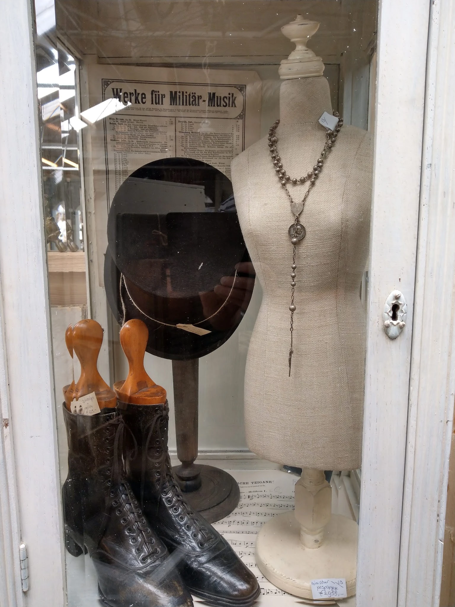 Vitrinekast met sieraden, een zwarte hoed op standaard en houten handschoenenhouders met bruine laarzen.
