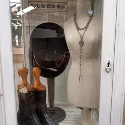 Vitrinekast met sieraden, een zwarte hoed op standaard en houten handschoenenhouders met bruine laarzen.