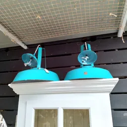 Twee turquoise industriële hanglampen op een witte plank tegen zwarte houten achtergrond