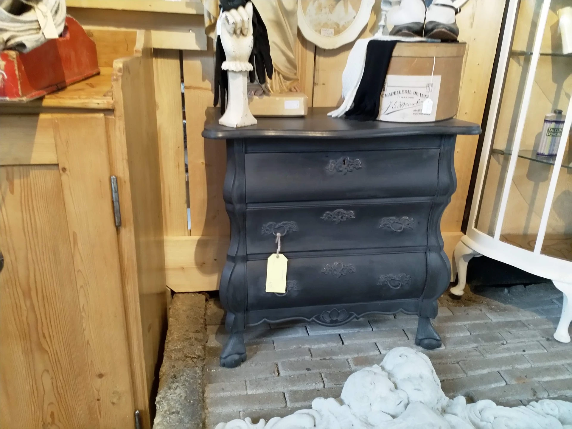 Zwarte vintage ladenkast met gebogen front en decoratieve details, uitgestald in de winkel