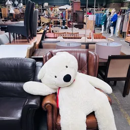 Grote witte pluche teddybeer zittend op een bruin lederen bank in een meubelshow
