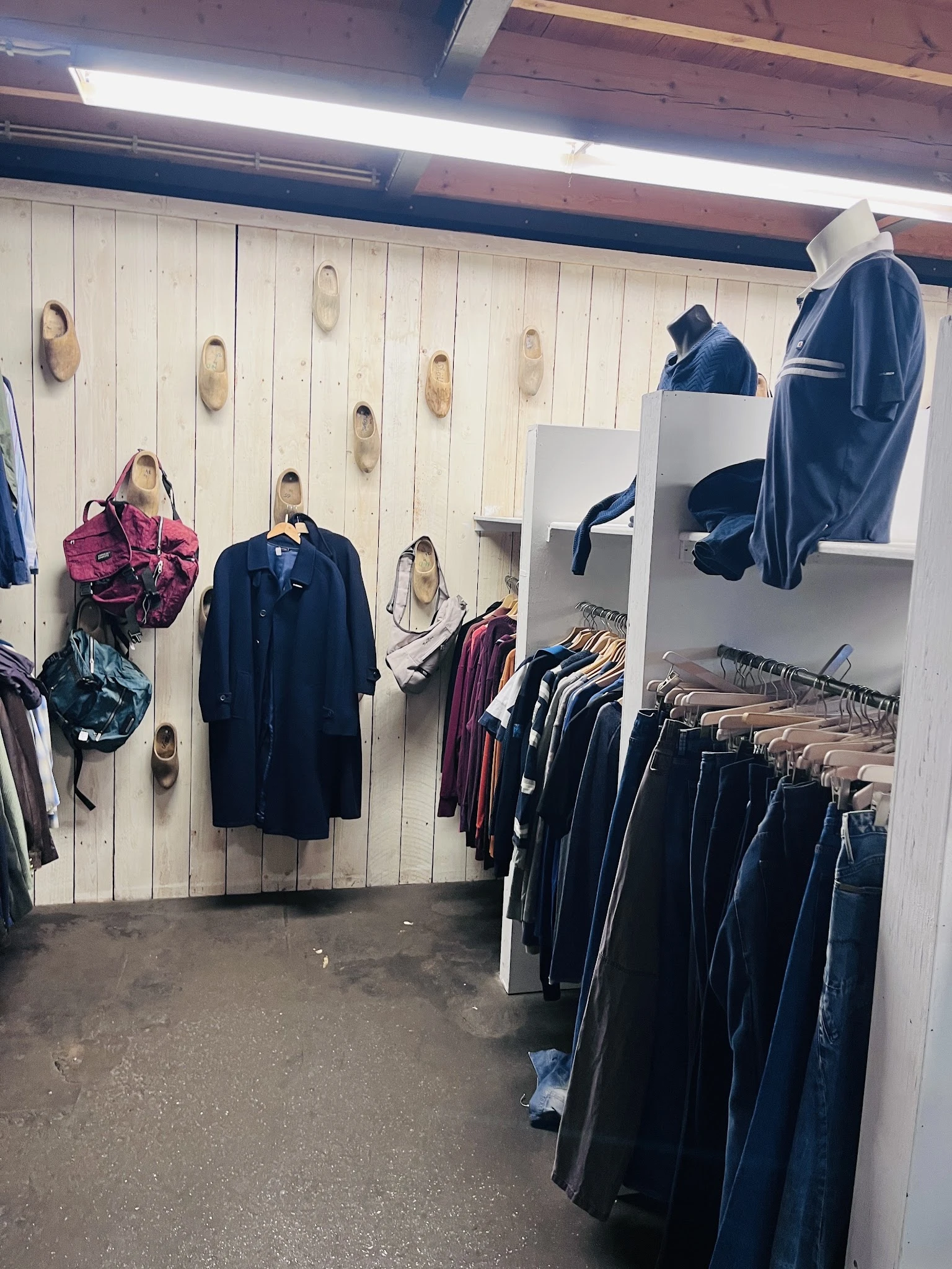 Rekken met tweedehands kleding, jassen en tassen aan de muur en stellingen in een kringloopwinkel