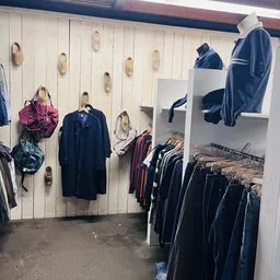 Rekken met tweedehands kleding, jassen en tassen aan de muur en stellingen in een kringloopwinkel