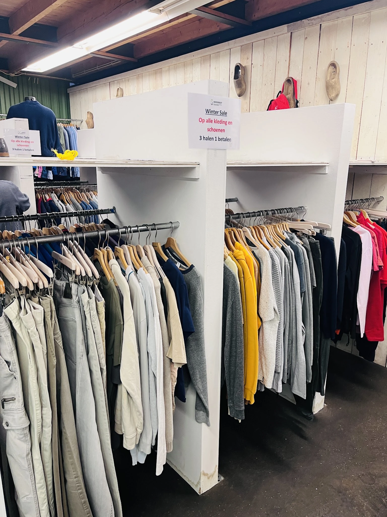 Rekken met tweedehands kleding in verschillende kleuren, waaronder geel, grijs, wit en zwart