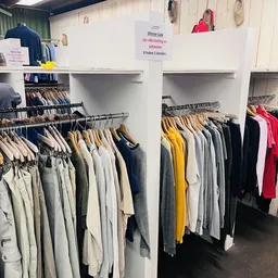 Rekken met tweedehands kleding in verschillende kleuren, waaronder geel, grijs, wit en zwart