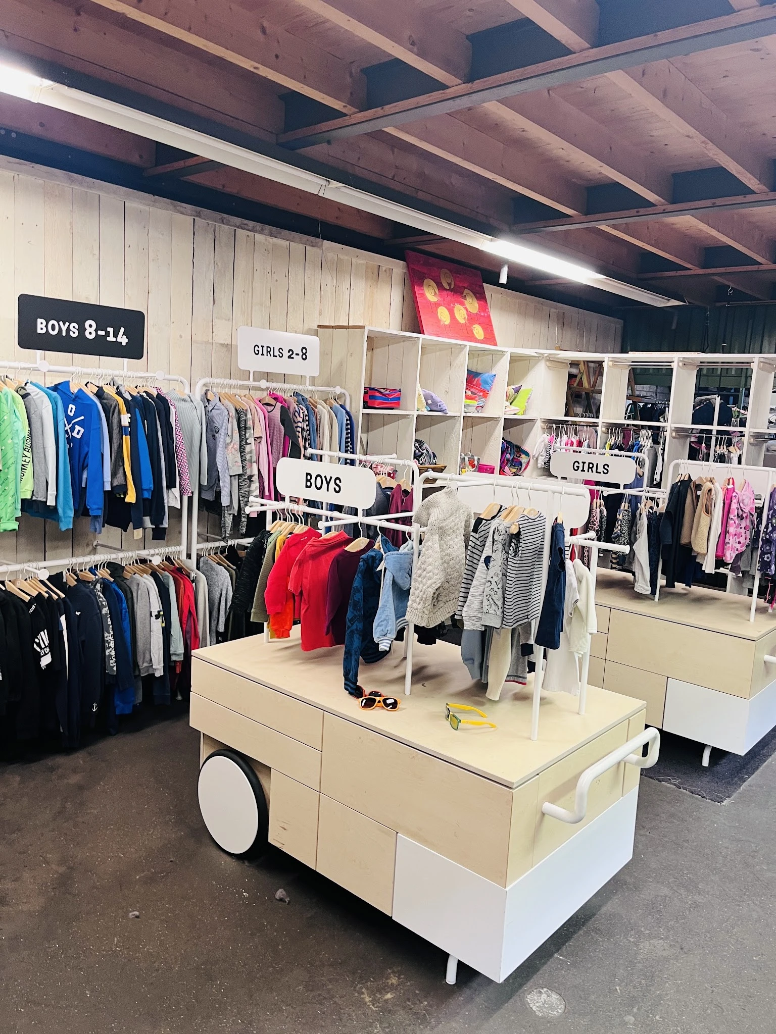 Kinderkleding op hangers en tafels, onderverdeeld in jongens- en meisjesafdelingen met duidelijke borden