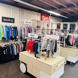 Kinderkleding op hangers en tafels, onderverdeeld in jongens- en meisjesafdelingen met duidelijke borden