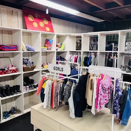 Witte stellingen met tweedehands kinderkleding, schoenen en accessoires in een kringloopwinkel, met een 'GIRLS' bord in het m