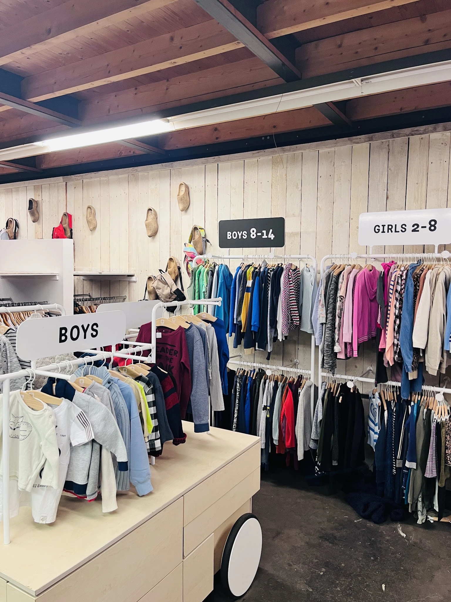 Kinderkleding op hangers, onderverdeeld in secties voor jongens en meisjes in een kringloopwinkel