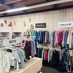 Kinderkleding op hangers, onderverdeeld in secties voor jongens en meisjes in een kringloopwinkel