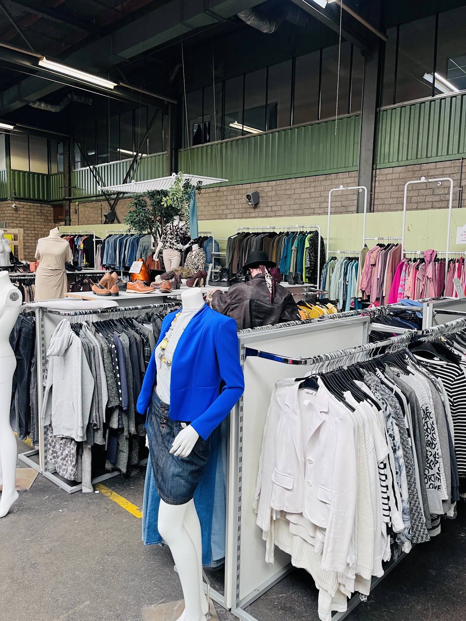 Rekken met tweedehands kleding, waaronder blauwe blazer, witte en gekleurde items in kringloopwinkel