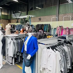Rekken met tweedehands kleding, waaronder blauwe blazer, witte en gekleurde items in kringloopwinkel