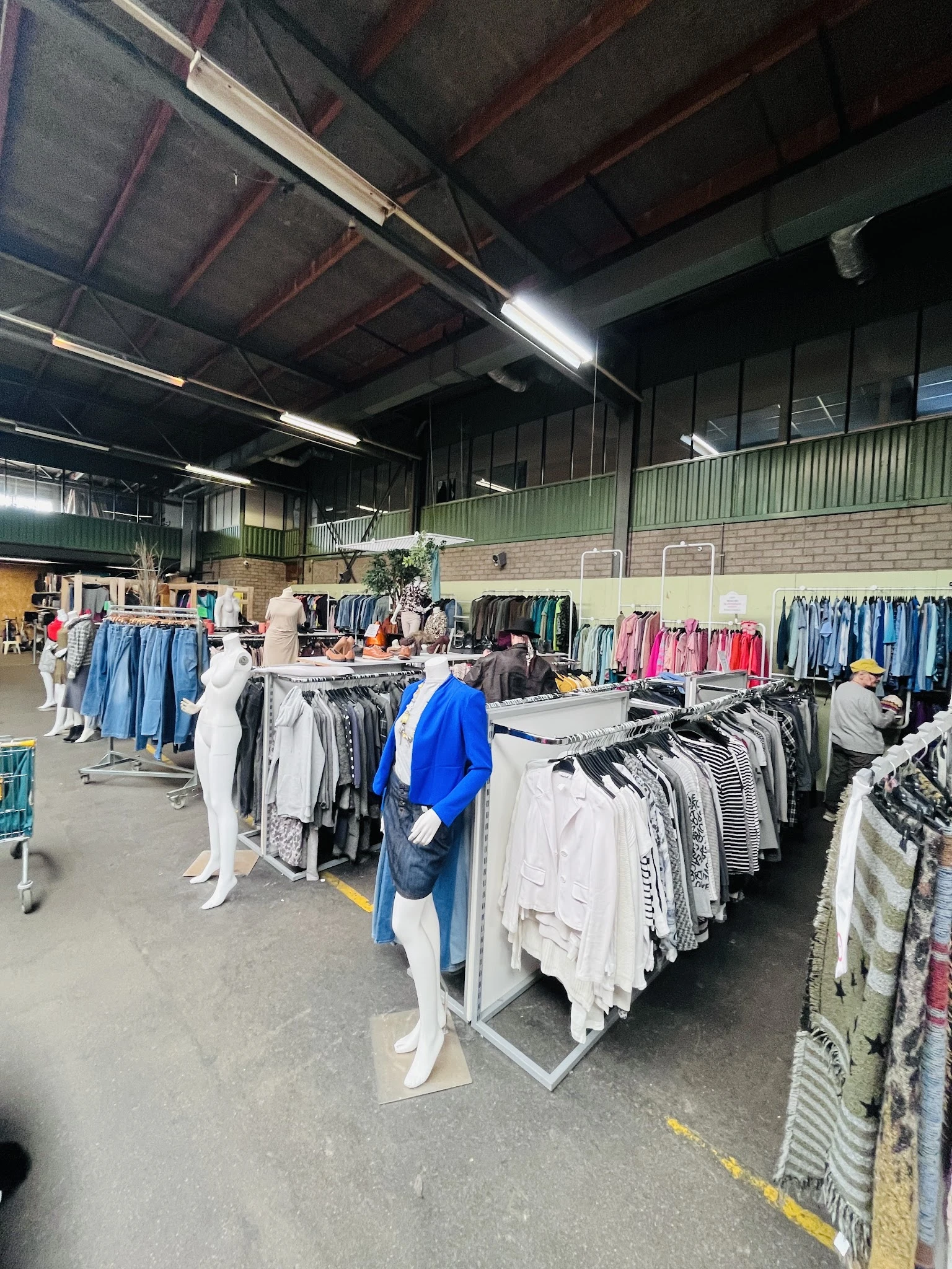 Winkelvloer met rekken vol tweedehands kleding, modepoppen en overzicht van de winkelafdeling