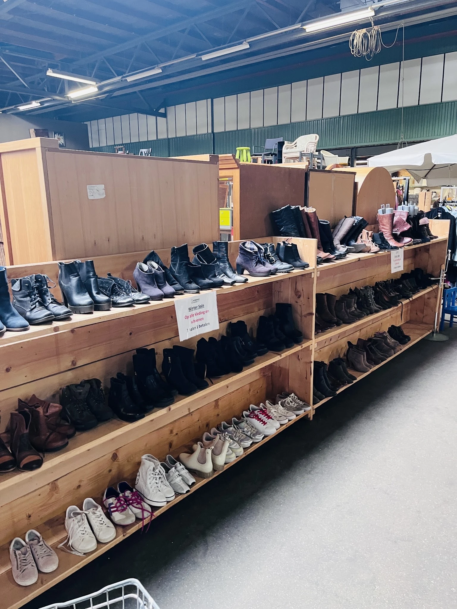 Houten stellingen met uitgestalde tweedehands schoenen en laarzen in verschillende kleuren en stijlen