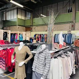 Rekken met tweedehands kleding, waaronder jassen, truien en blouses op hangers in de winkelruimte