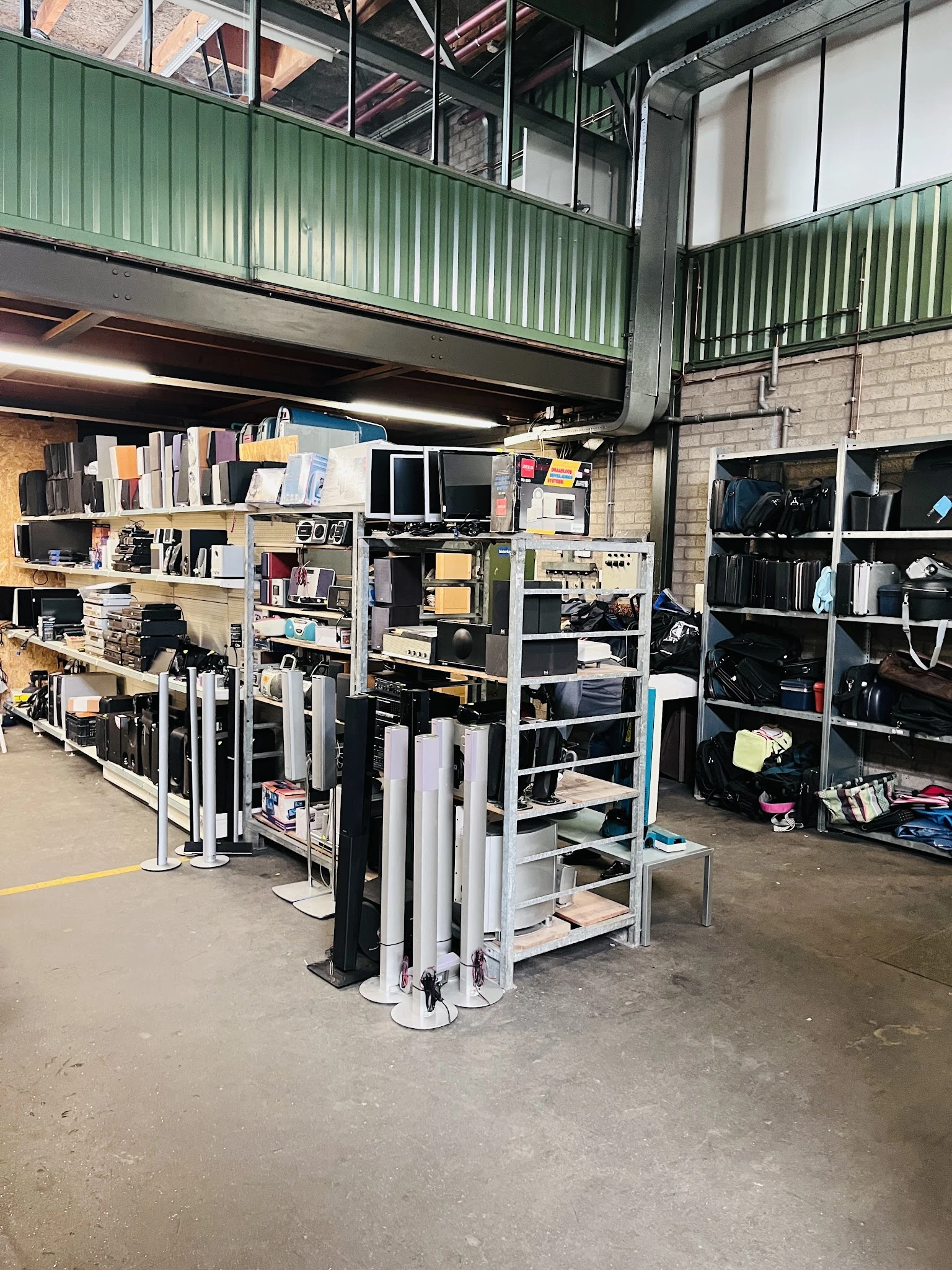 Stellingen met diverse elektronische apparaten, monitoren en huishoudelijke items in een kringloopwinkel