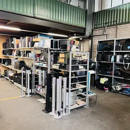 Stellingen met diverse elektronische apparaten, monitoren en huishoudelijke items in een kringloopwinkel