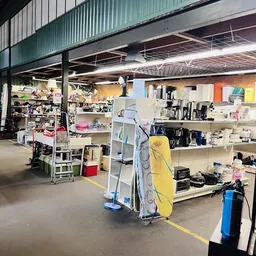 Winkelvloer van kringloopwinkel met stellingen, kasten en diverse spullen uitgestald, inclusief een geel surfboard