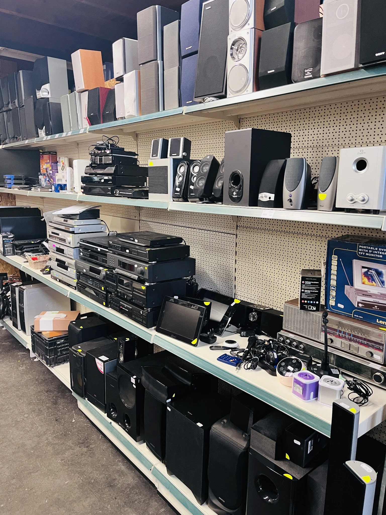 Stellingen met elektronische apparatuur: speakers, versterkers, dvd-spelers en digitale apparaten in een kringloopwinkel