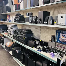 Stellingen met elektronische apparatuur: speakers, versterkers, dvd-spelers en digitale apparaten in een kringloopwinkel
