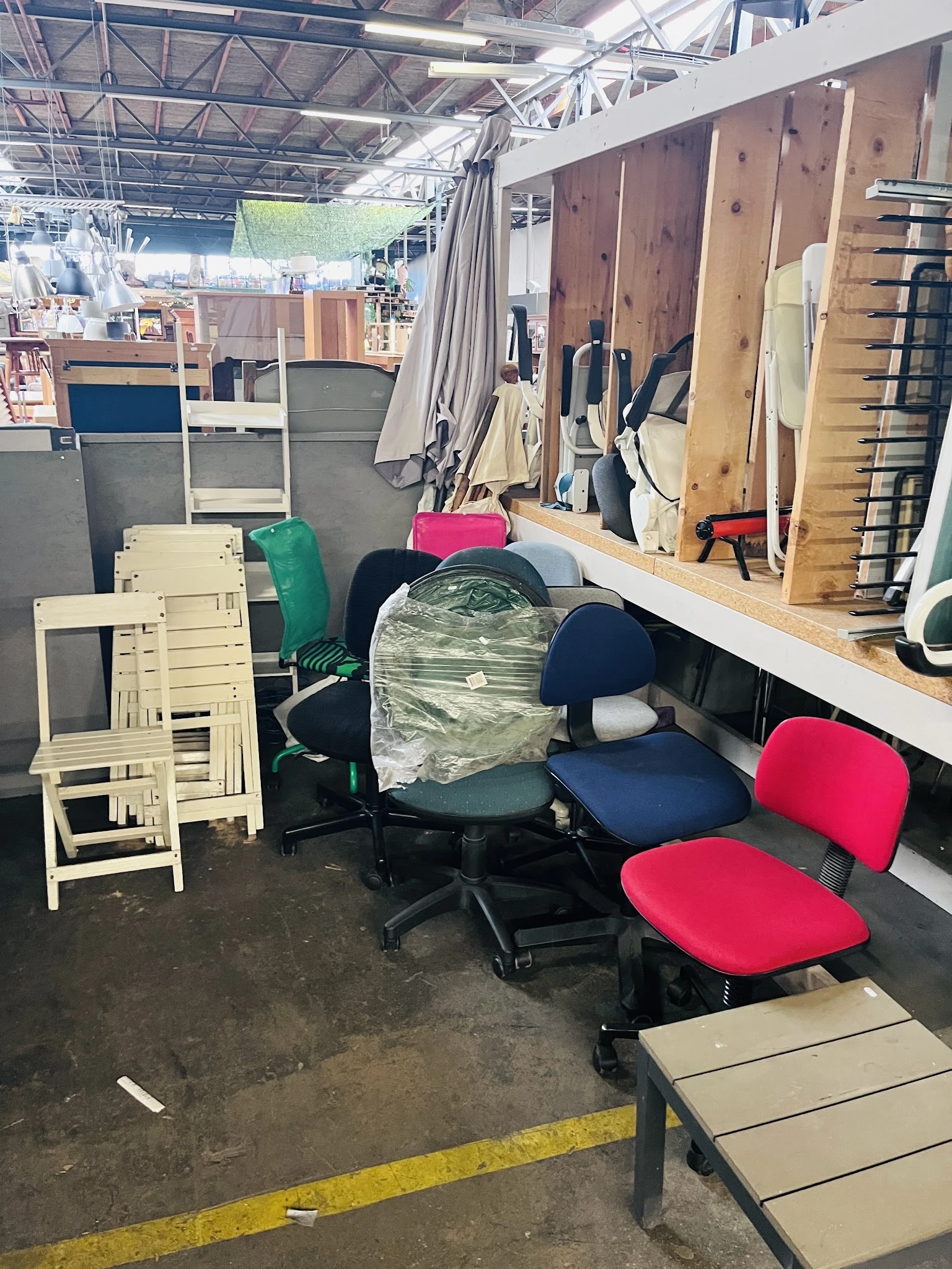Diverse gebruikte meubels en stoelen in een kringloopwinkel, waaronder witte klapstoelen, bureaustoelen met rode en blauwe be