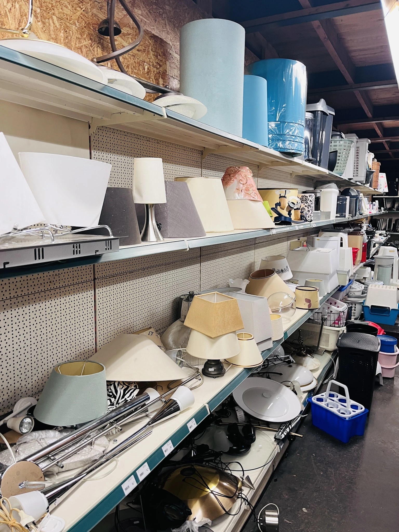 Stellingen met diverse huishoudelijke artikelen zoals lampen, servies en keukengerei in een kringloopwinkel